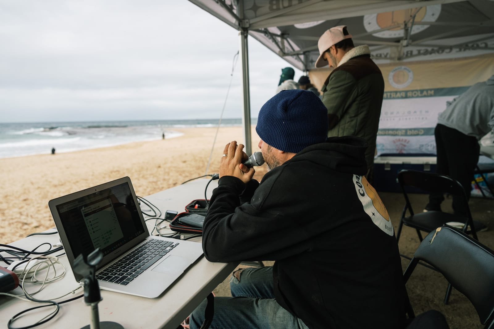 A judge scoring heats on a laptop under the club marquee, facing the surf