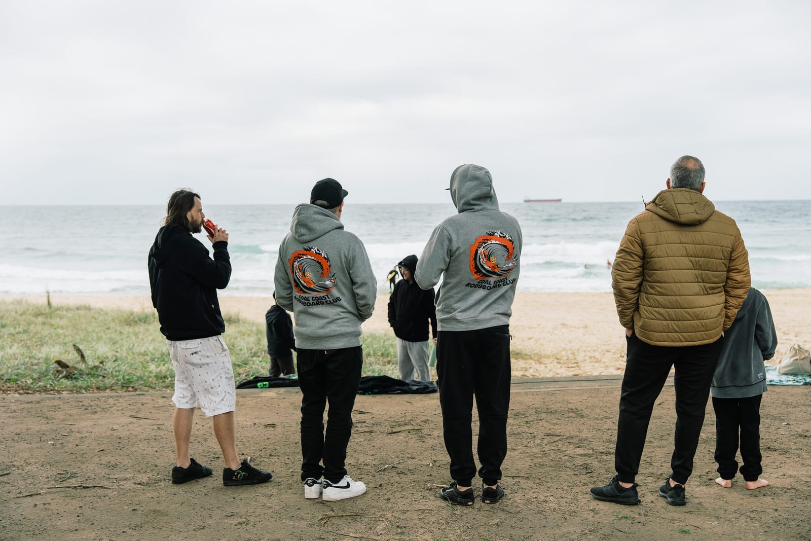 Club members in CCBC hoodies watching the heats from the edge of the sand